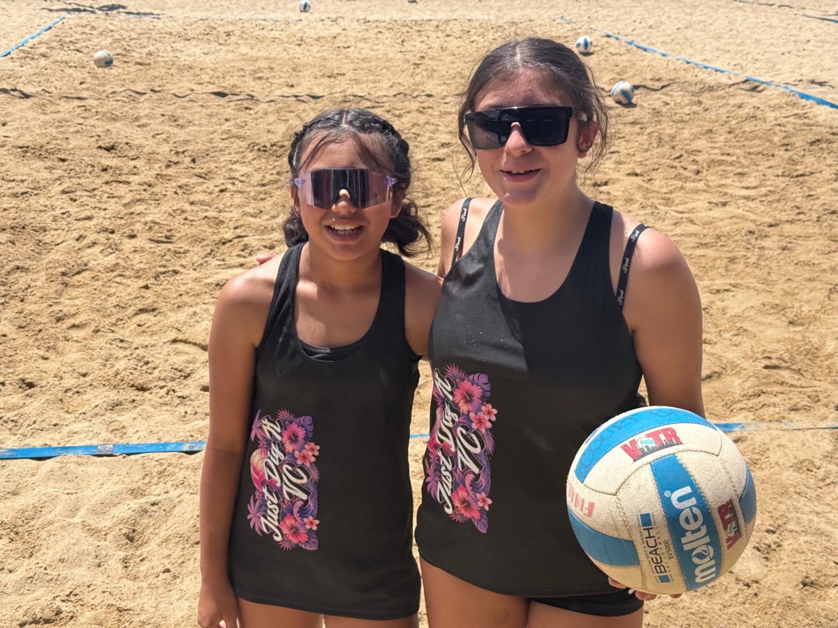 Two Just Dig It VC players on the outdoor sand court with a beach volleyball