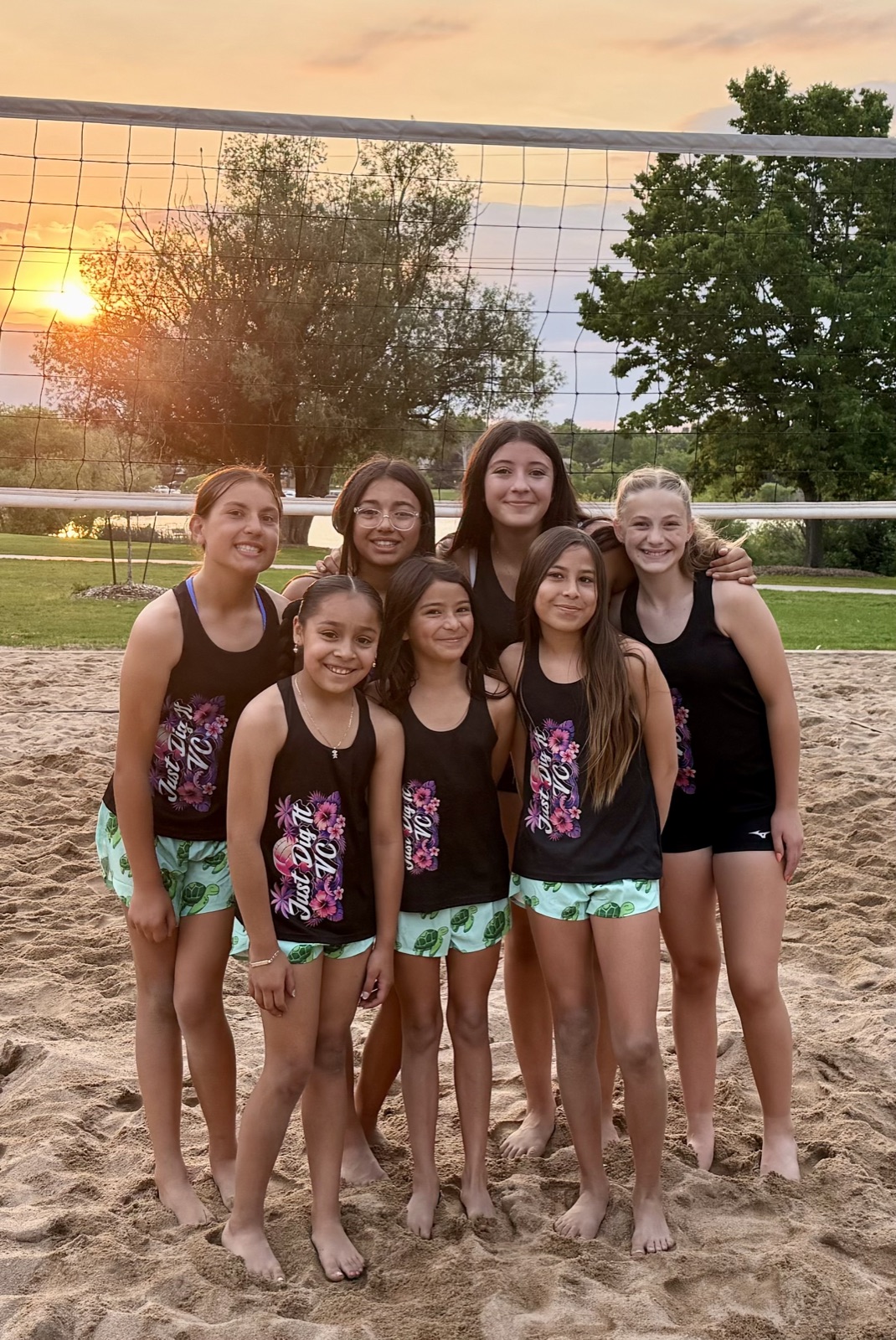 Just Dig It VC Beach team posing together at the net during a sunset tournament